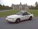 1993 Ford Mustang - A white police car is parked on asphalt with a large building in the background.