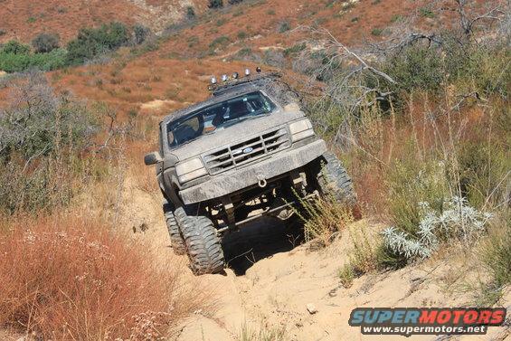 1992 Ford Bronco climbing a steep, sandy hill with dry brush and trees