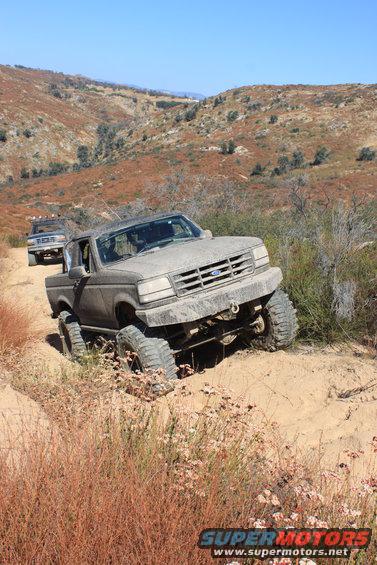 Gray Ford F-Series truck on a dirt trail, front wheel deep in sand, lifted suspension, off-road tires