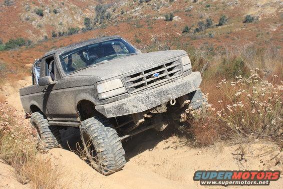 1992 Ford Bronco climbing a dirt trail, covered in mud