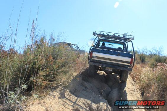 Dark blue Ford Bronco with a roof rack navigates a steep, rocky incline