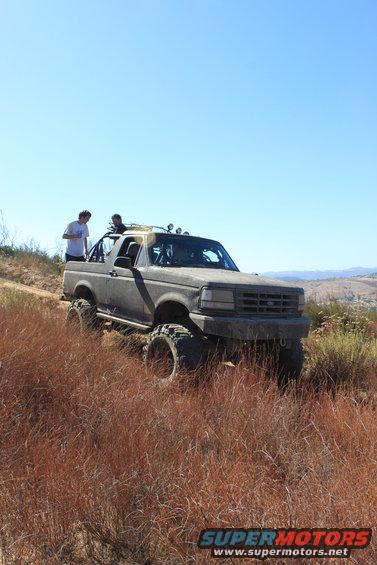 Gray 1992 Ford Bronco with large tires and off-road lights on a dirt trail
