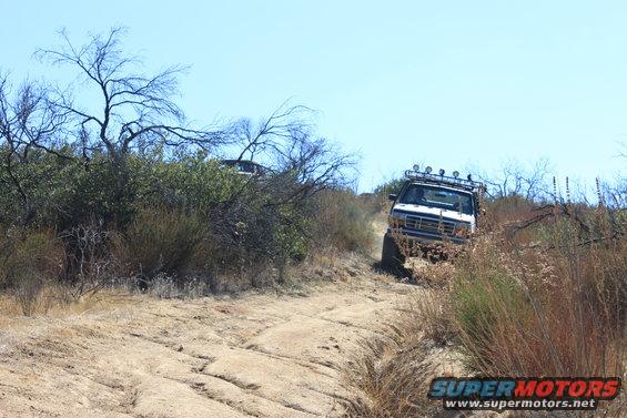 White SUV with roof rack and lights driving on a dirt trail