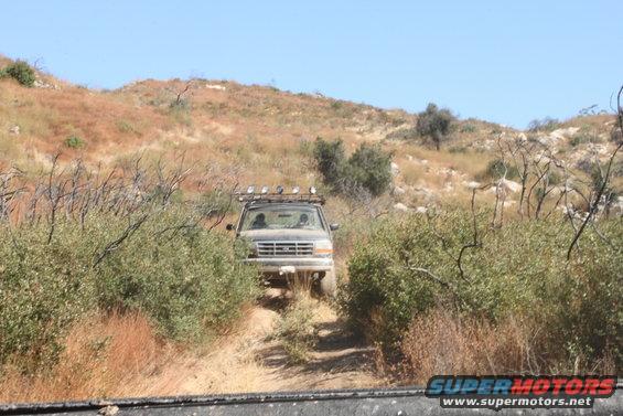 1992 Ford Bronco driving on a dry, overgrown trail with hills in the background
