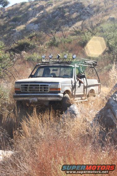 Ford F-Series truck with roof rack and off-road lights driving on a rocky trail