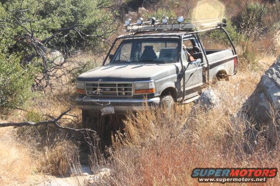 Modified Ford F-Series truck with roll cage and roof lights on a dry, grassy trail