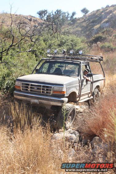 Gray 1992 Ford Bronco on rocky trail with roof rack and lights