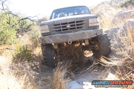 Ford Bronco climbing over rocks on a dry, brushy trail. Front view