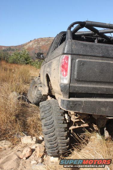 1992 Ford Bronco with large tires on a rocky, dry trail, rear view