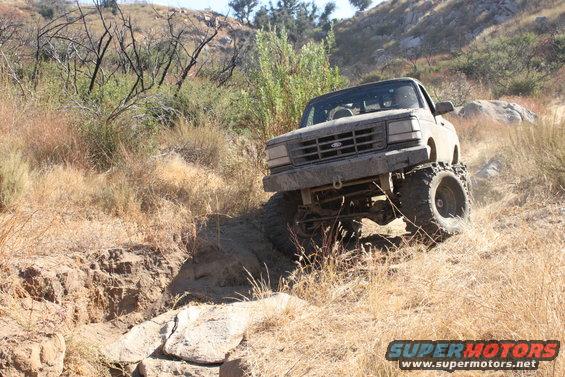 Mud-covered 1992 Ford Bronco climbing a rocky, dry hillside with large tires