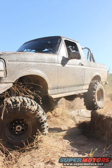 Mud-covered 1992 Ford Bronco climbing a dirt embankment with large off-road tires