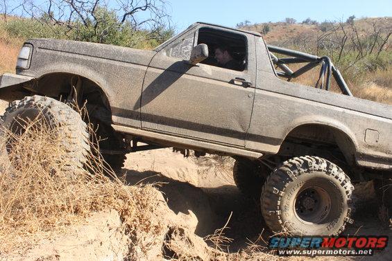 Modified 1992 Ford Bronco with large tires climbing a dirt hill
