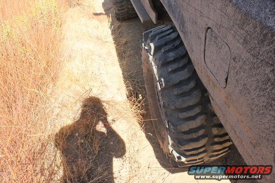 Shadow of person taking photo next to large off-road tire on dirt path