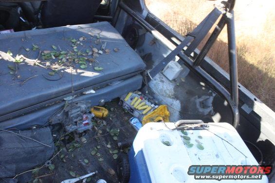 Interior of a vehicle with seats, a cooler, and debris scattered around. A roll cage is visible