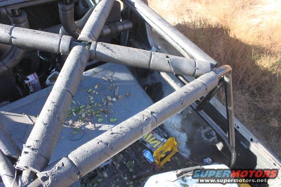 Interior view of a vehicle with a roll cage, some debris on the floor, and a yellow container