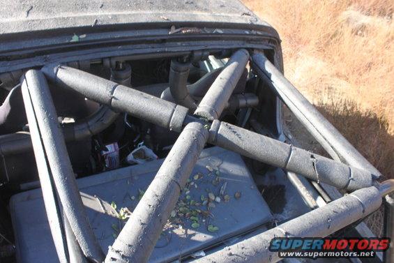 Damaged vehicle interior with a prominent roll cage, engine components visible, and debris scattered