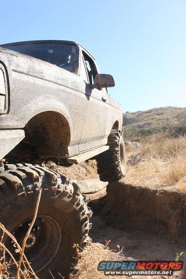 Mud-covered 1992 Ford Bronco with large off-road tires climbing a dirt embankment
