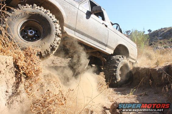 Gray 1992 Ford Bronco climbing a dirt embankment, kicking up dust