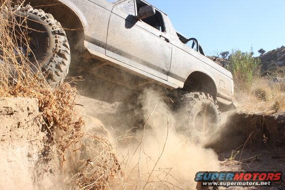 Off-road vehicle kicking up dust while climbing a steep dirt trail