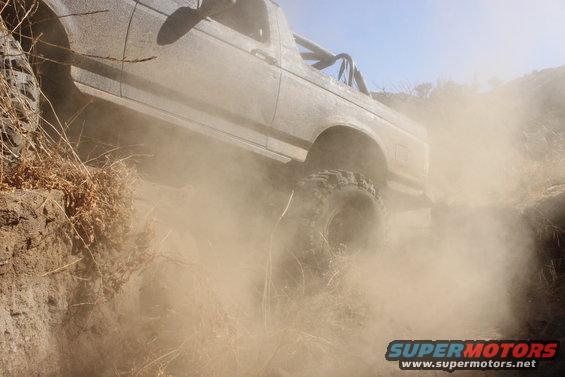 Silver 1992 Ford Bronco driving through dust on a dirt trail