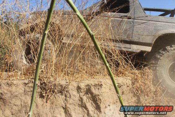 1992 Ford Bronco driving through dry brush on a dirt embankment