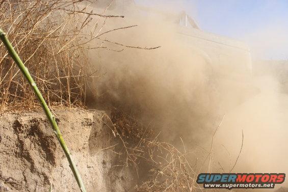 Off-road vehicle driving through dry brush, kicking up a large dust cloud