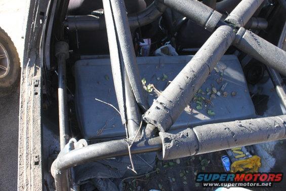 interior view of a vehicle with a roll cage, showing a gray storage bin and debris on the floor