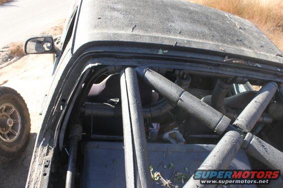 Roll cage inside a dusty off-road vehicle, side mirror visible