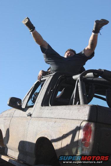 Dirty 1992 Ford Bronco with a man on top, viewed from the front-right