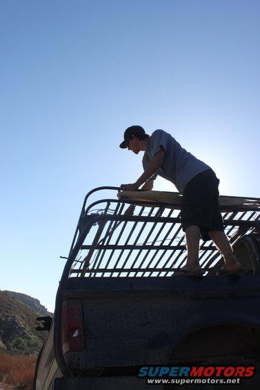 Man on roof rack of dark truck, clear blue sky