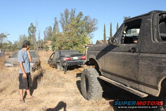 Mud-covered 1992 Ford Bronco, 3/4 front view, with a damaged black car behind it
