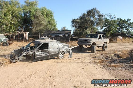 Lifted pickup truck towing a heavily damaged sedan on a dirt road