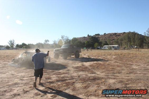 Two trucks in a dusty field with a person walking