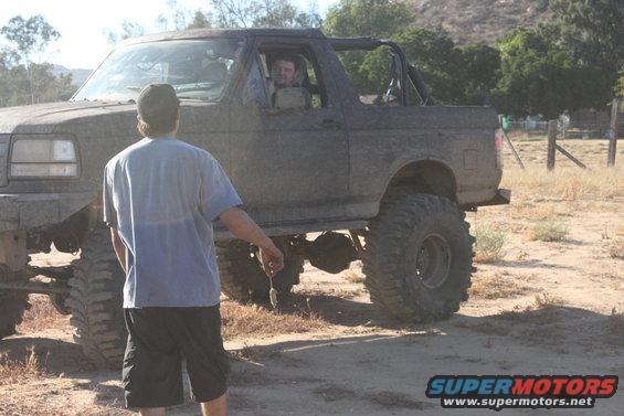 Muddy 1992 Ford Bronco with large tires, lifted suspension, and a roll cage visible. Driver is in the cab