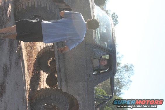 Side view of a heavily modified off-road vehicle with large tires and a person in the driver's seat