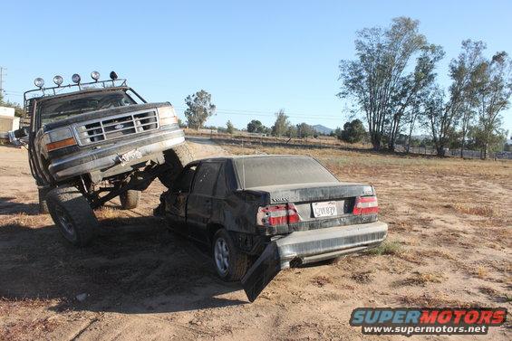 Black Ford F-Series truck crushing a dark sedan in a dirt lot