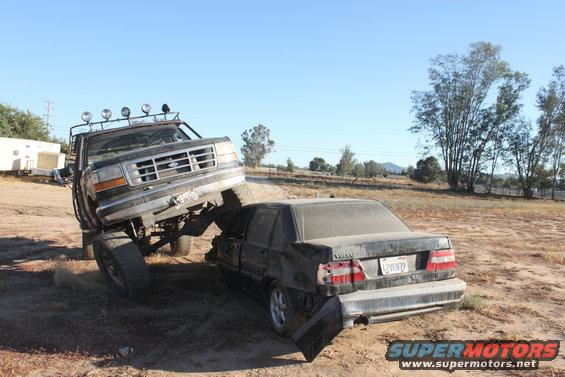 1992 Ford Bronco crushing a black Volvo sedan in a dirt lot