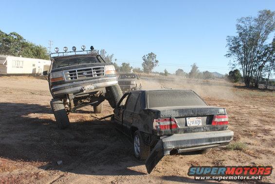 Lifted 1992 Ford Bronco on a sedan in a dusty outdoor scene