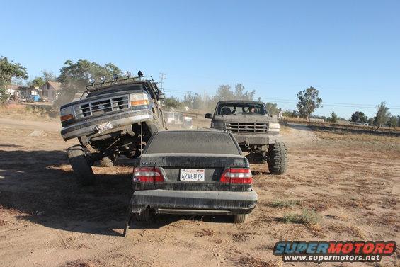 Lifted 1992 Ford F-150 on left, another lifted Ford truck behind it, and a Volvo sedan in front. Dirt lot scene