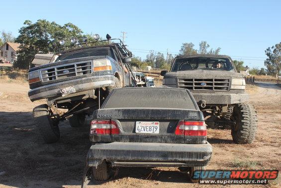 1992 Ford Bronco lifted high, another lifted Ford truck, and a Volvo sedan parked together