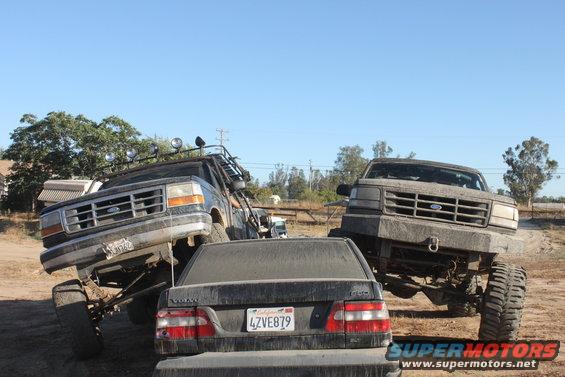Two lifted 1992 Ford Broncos and a Volvo sedan on a dirt lot