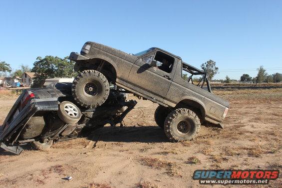 Muddy 1992 Ford Bronco on top of a crushed car, off-road