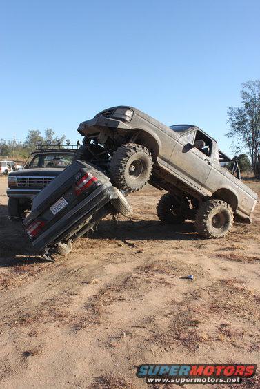 1992 Ford Bronco on top of a crushed sedan, another Bronco in background