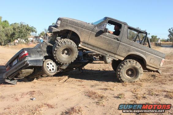 1992 Ford Bronco crushing a sedan on a dirt trail