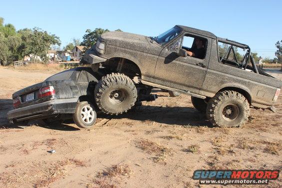 Muddy lifted truck on top of a crushed sedan
