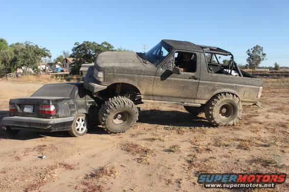 1992 Ford Bronco crushing a black sedan on a dirt road
