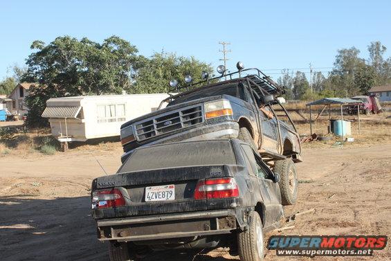 1992 Ford Bronco with roof rack on top of a black Volvo sedan, license plate 4ZVE879