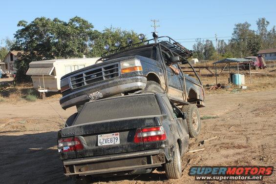 1992 Ford Bronco on top of a black Volvo sedan, both vehicles dirty, in a rural setting