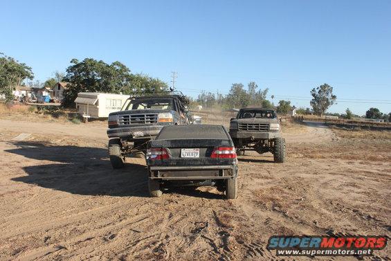 Three lifted trucks in a dusty outdoor area, one in foreground