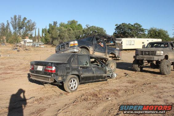 1992 Ford Bronco on top of a black sedan, with another Ford Bronco in the background